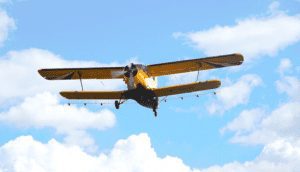 Yellow single engine biplane with blue sky and white clouds in background